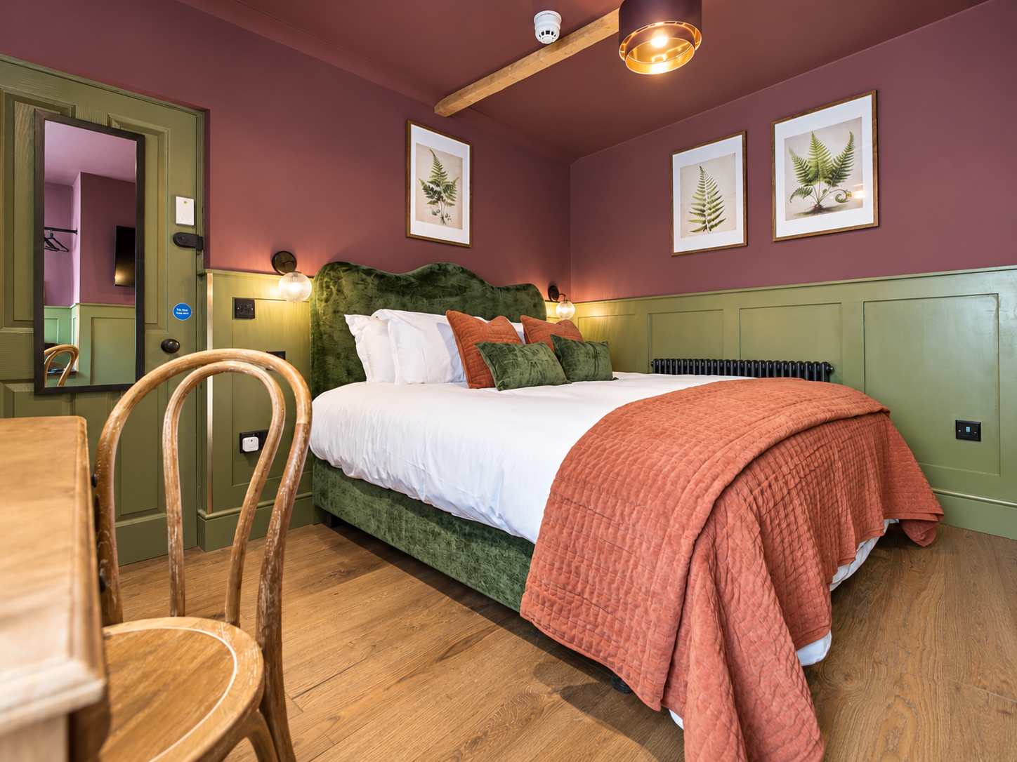Room 2 at The Linen Rooms — bed with a sage green headboard, lit vanity mirror by the window and the green-tiled ensuite beyond
